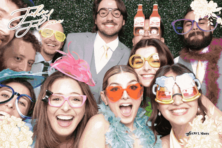 A wedding reception boomerang moment against a greenery backdrop, complete with novelty prop glasses