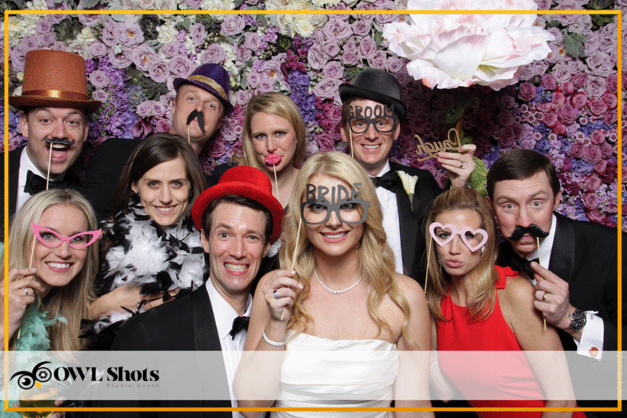 A wedding reception moment inside a floral photo booth backdrop, complete with Bride and Groom signs