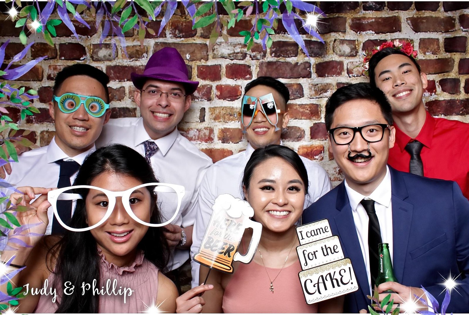 Judy and Phillip's wedding celebration under a brick-wall backdrop, complete with playful prop signage